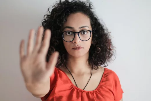 portrait photo of woman in red top wearing black framed eyeglasses holding out her hand in stop gesture